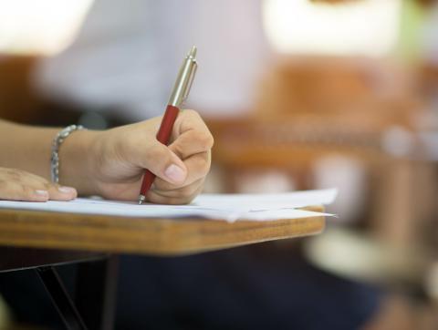 Closeup to hand of student holding pen and taking exam in cl